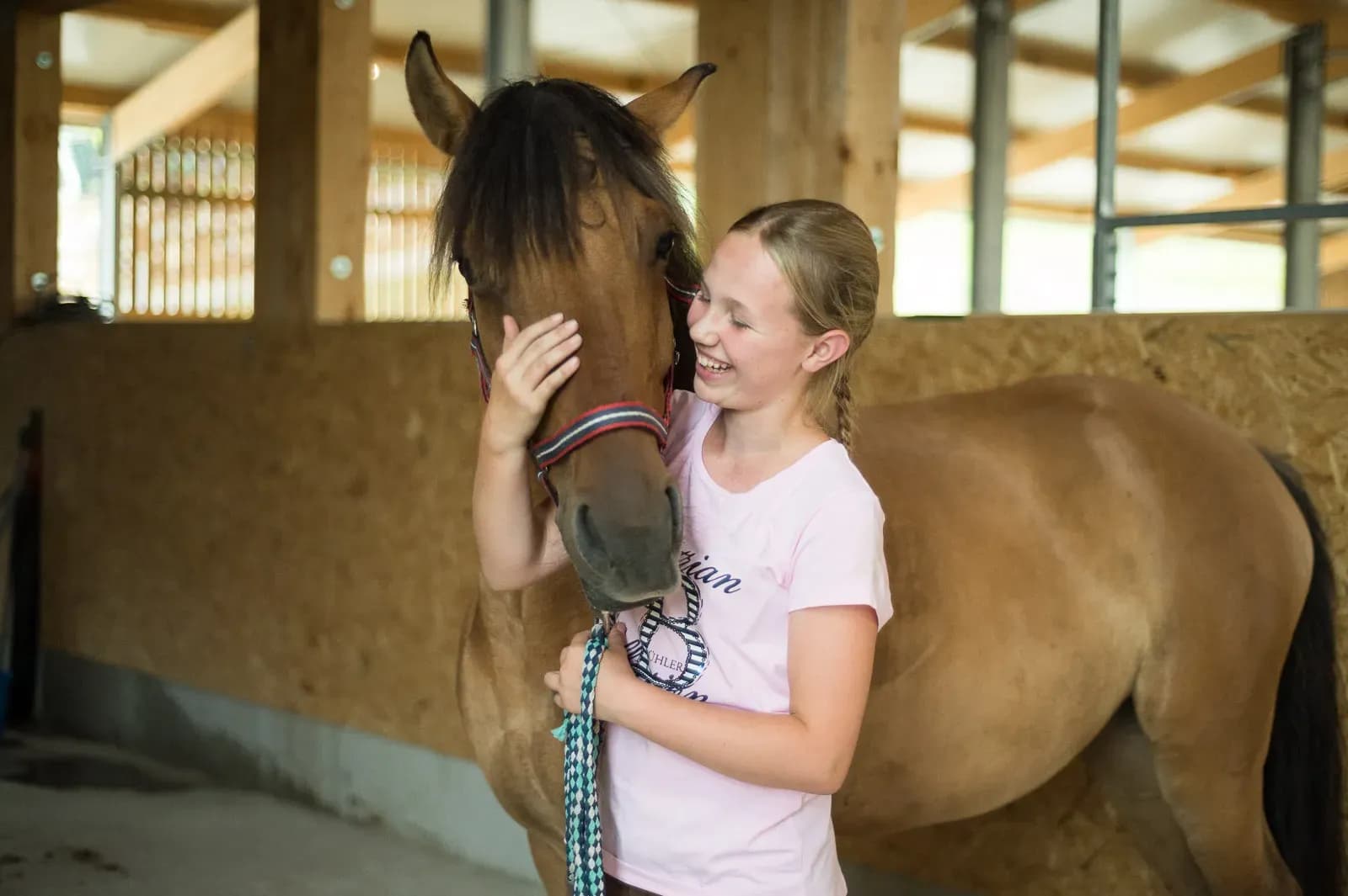 Glücklich lachendes Mädchen, während Sie mit einem der Pferde auf dem Schreinerhof kuschelt. 